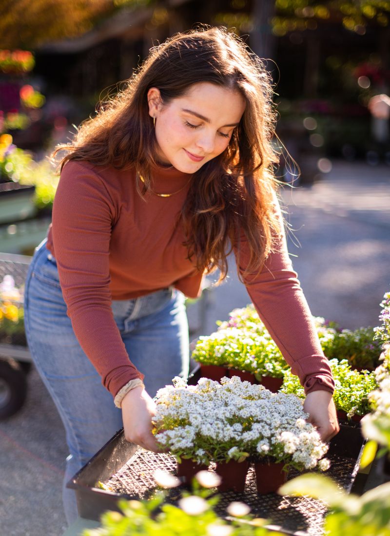 CNF Web 800x1100px (1) A woman smiling and picking up white flowers.